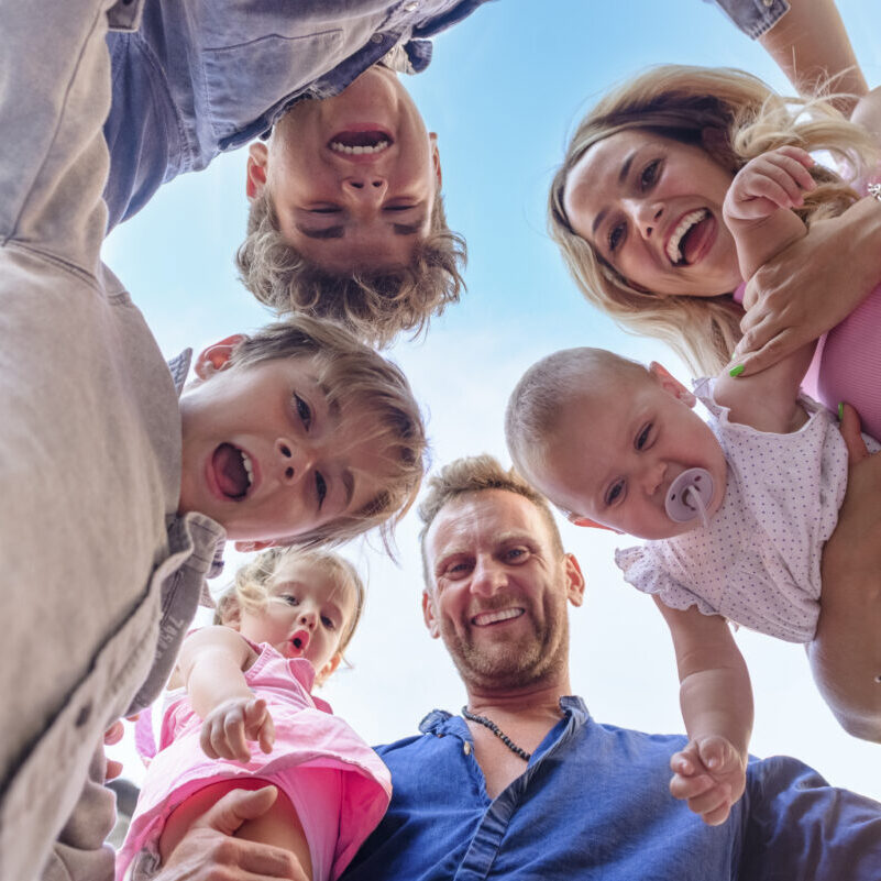 shot from below of a young adult family time having fun outdoors. mom and dad portrait carrying kids on holiday with children. cropped low view of happy people. joy, togetherness and lifestyle concept