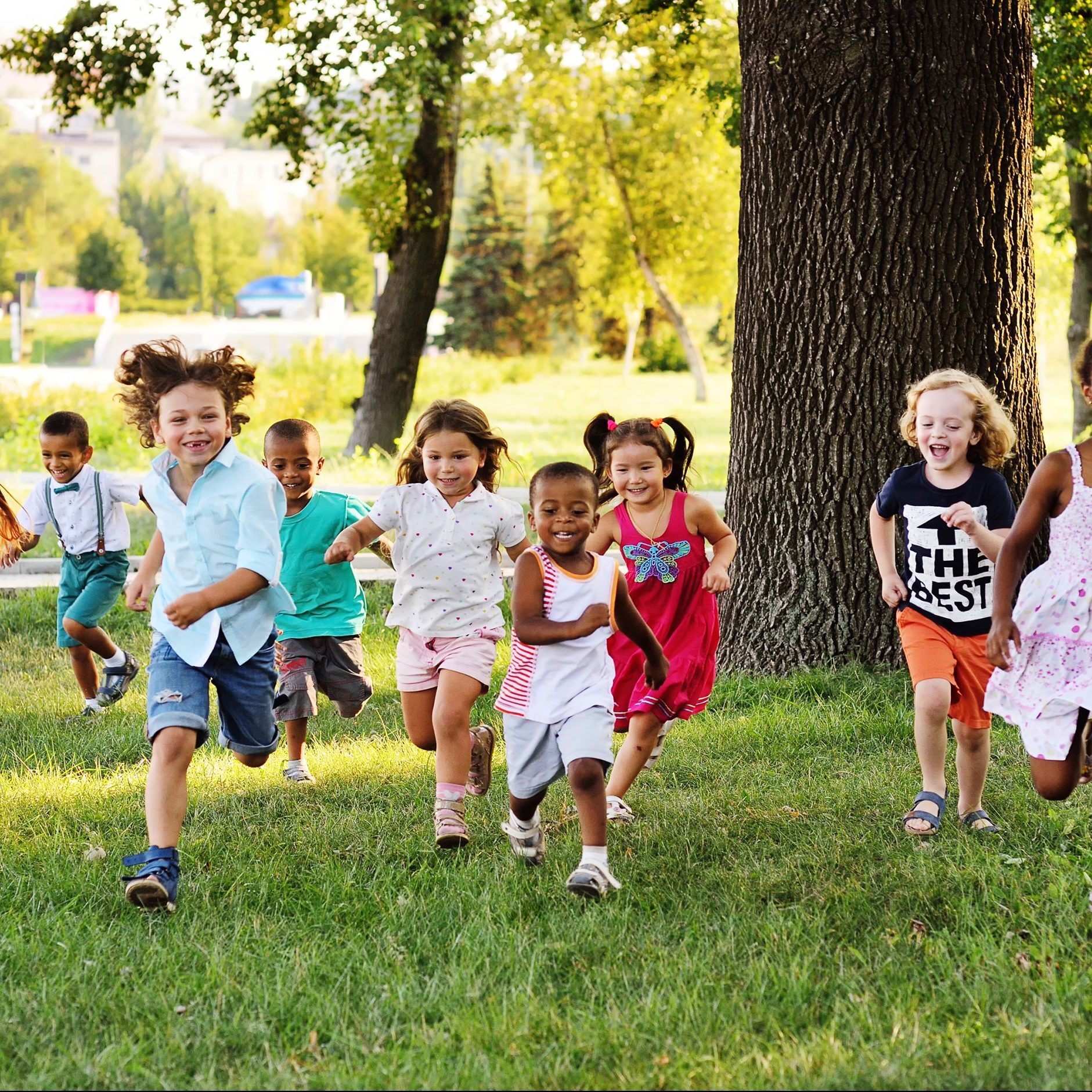 A group of happy children of boys and girls run in the Park on the grass on a Sunny summer day . The concept of ethnic friendship, peace, kindness, childhood.